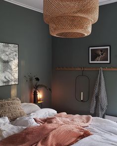 an unmade bed in a bedroom with a wicker basket hanging from the ceiling