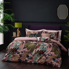 a bed with pink and green leaves on it in a room next to a plant