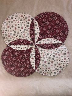 four circular quilts are arranged on a white surface with red and grey flowers in the center