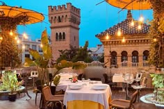 an outdoor dining area with tables, chairs and umbrellas over looking the city at dusk