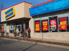 two people are walking past a store that sells coupons and other items on the sidewalk