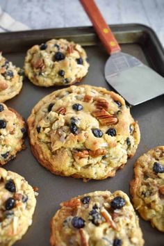 several cookies with blueberries and pecans are on a baking sheet next to a spatula