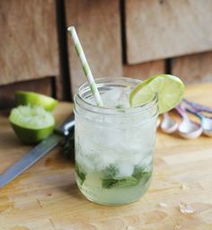 a mason jar filled with ice and limes next to a knife on a cutting board