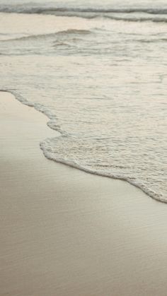 a person walking on the beach with their surfboard in hand and water coming up from the shore