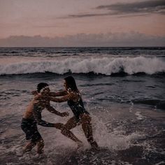 two people are playing in the water at the beach