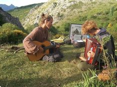 two women sitting in the grass playing an instrument