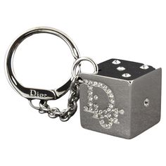 DIOR RHINESTONE GAMBLER DICE KEYRING KEYCHAIN The large square shiny reflective silver tone dice has the Dior name logo on two sides and the pips 1,2,3 and 5. Everything is set with bright clear rhinestones. A thick chain is attached to a round key holder that has a hinged lever closure. A larger size, the dice measures 1 inch square. The ring is 1 3/8 inch in diameter and the chain is 2 inches long. Color: Silver tone Material: metallic Marks: Brand mark Clasp Style: Year: 2004 Measures: 2 x 2 Luxury Silver Enamel Pin, Luxury Edgy Jewelry Gift, Stussy 8 Ball Keychain, Chrome Hearts Decor, 2000s Keychains, Dior Keychain, Rich Gifts, Accessory Inspo, Brand Mark