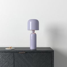 a purple lamp sitting on top of a black cabinet next to a white wall and floor