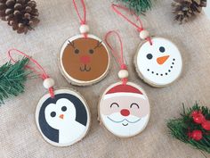 four wooden ornaments with christmas decorations on them and pine cones in the background, including one penguin