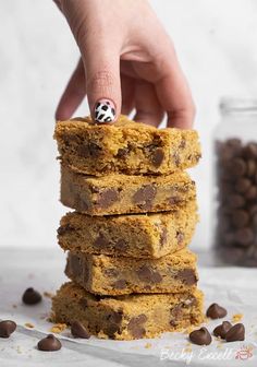 a stack of chocolate chip cookie bars with a person's finger on one of them