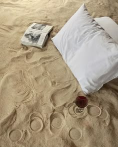 an empty bed with two pillows and a book on the floor next to it, which is covered in sand