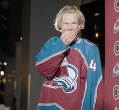 a young man covers his mouth while standing in front of a red and blue hockey jersey