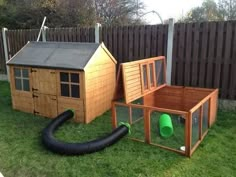 an outdoor play area with a dog house, water hose and chicken coop in the grass