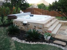 a hot tub sitting in the middle of a yard next to a stone wall and steps