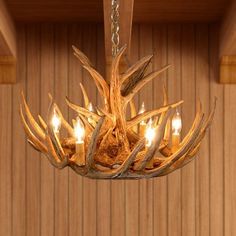 a chandelier made out of antlers with candles in the center and wood paneled wall behind it