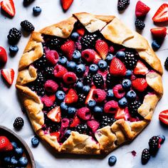 a pie with berries, blueberries and raspberries on it is surrounded by other fruit