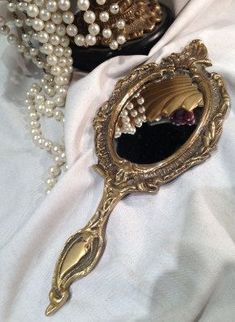 an ornate mirror with pearls on it sitting on a white cloth next to other items