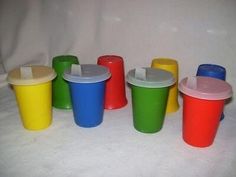 plastic cups with lids are lined up on a white tableclothed surface in different colors