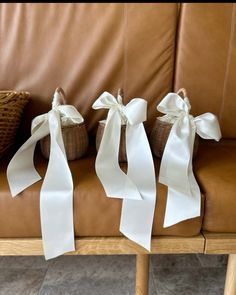 three baskets with white ribbons tied to them on a brown leather couch next to a wicker basket