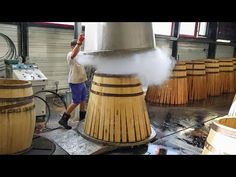 a man standing next to wooden barrels with steam coming out of them and spraying water on them