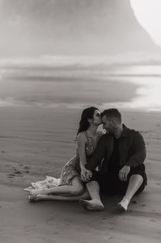 a man and woman sitting on the beach kissing