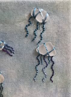 three pieces of art made out of wire and glass beads on a gray cloth background