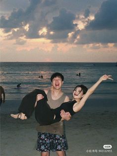 two people are standing on the beach with their arms in the air and one person is holding another