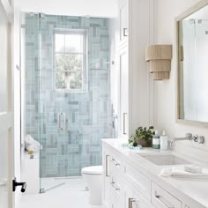 a white bathroom with blue tiles on the shower wall and vanity, toilet and sink