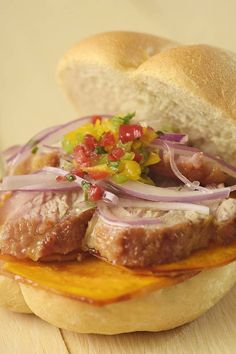 a sandwich with meat, onions and salsa on it sitting on a wooden table next to a roll