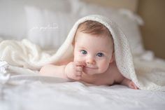 a baby laying on top of a bed under a blanket covered in a white blanket