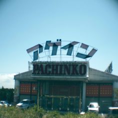 an old fashioned movie theater with cars parked in the parking lot behind it and a sign that says pachinko