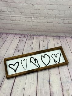 a wooden sign with hearts drawn on it in front of a brick wall and floor