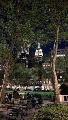 people sitting at tables in the middle of a park with skyscrapers in the background