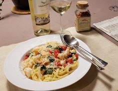 a white plate topped with pasta next to two bottles of wine