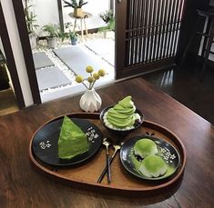 a wooden table topped with two black plates filled with green desserts on top of it