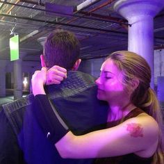 a man and woman embracing each other in a room with purple lights on the ceiling