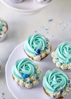 four cupcakes with blue frosting and sprinkles on a white plate