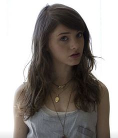 a woman with long hair wearing a necklace and looking off to the side while standing in front of a window