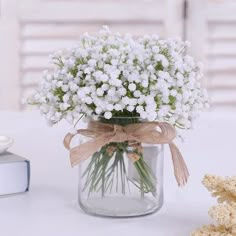 a glass jar filled with white flowers on top of a table next to a book