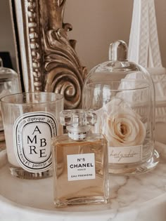 two bottles of perfume sitting on top of a marble table next to a mirror and vase