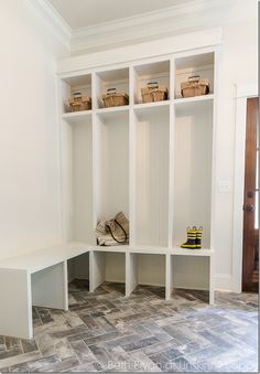 a white bench with baskets on it in front of a wall mounted shelf and door