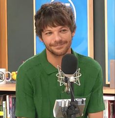 a man in a green shirt is talking into a microphone and smiling at the camera