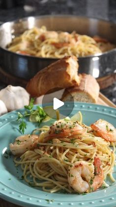 a blue plate topped with pasta and shrimp next to garlic bread on a wooden table