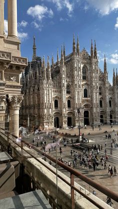 many people are walking around in front of an old building with tall towers and spires