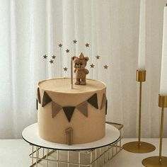 a cake with a teddy bear sitting on top of it next to two gold candles