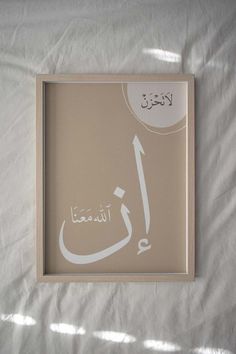 an arabic calligraphy is displayed in a frame on a white sheeted surface with sunlight coming through the window