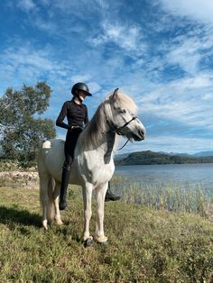 a woman riding on the back of a white horse next to a body of water