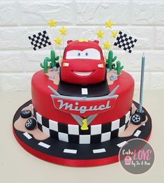 a red cake with cars on it sitting on top of a table next to a white brick wall