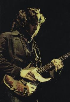 a man with long hair playing an electric guitar