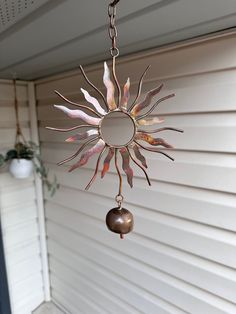 a metal sunburst hanging from a chain on a house porch with a potted plant in the background